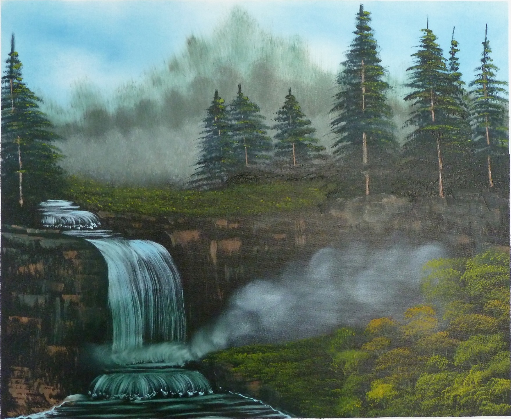 Wasserfall über Felsen vor nebelverhangenem Nadelwald.